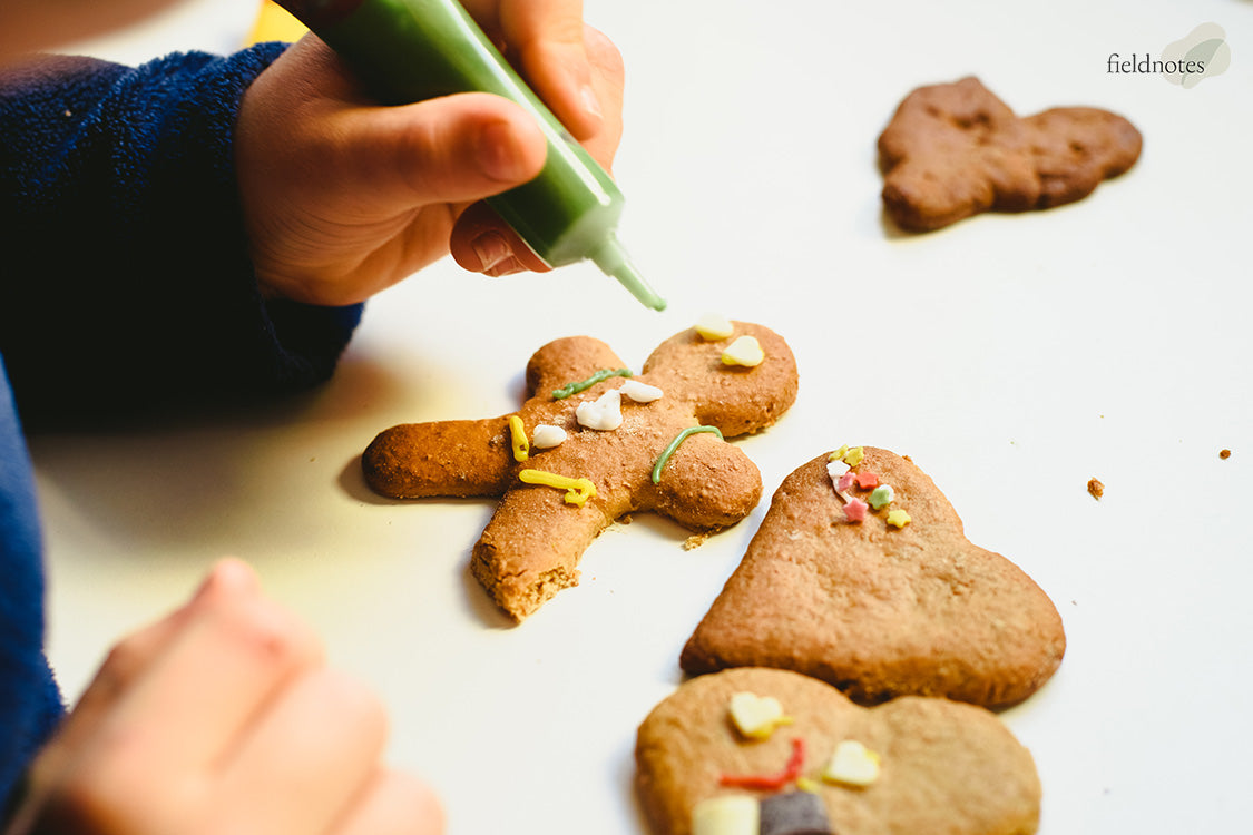 A person decorating a gingerbread man cookie with green icing.