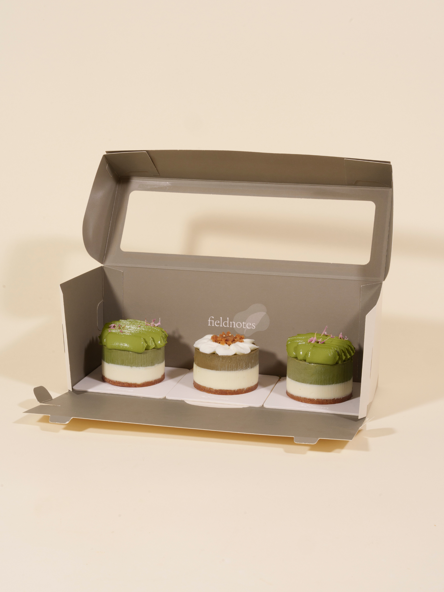 Three small cheesecakes, like birthday cake or tart flavors, in a fieldnotes box show green, white, and brown layers.