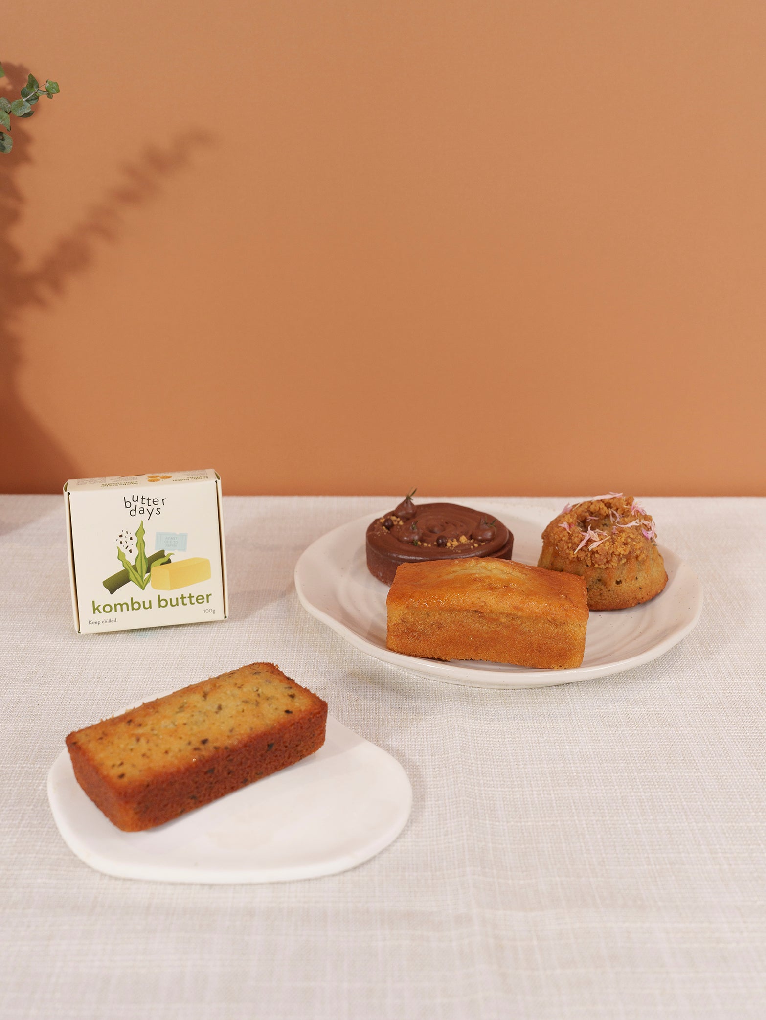 The Fieldnotes x Butter Days Quiet Warmth Box shows kombu butter, a tart, birthday cake, and a loaf slice on a white tablecloth.