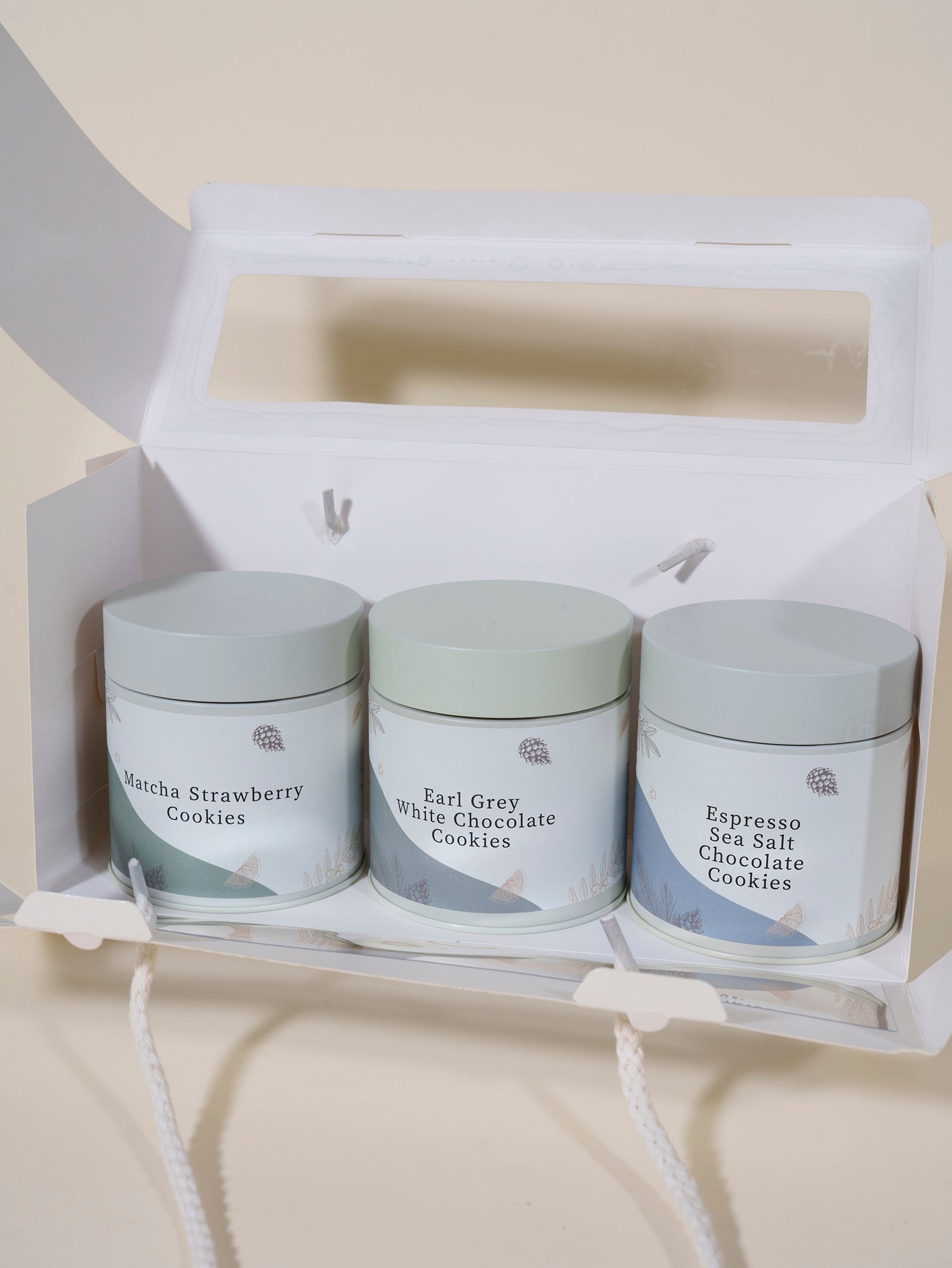 The fieldnotes Days of Wonder | Assorted Cookies Set features three pastel tins—Matcha Strawberry, Earl Grey White Chocolate, and Espresso Sea Salt Chocolate cookies—plus a birthday cake tart—in an open white gift box with a handle.
