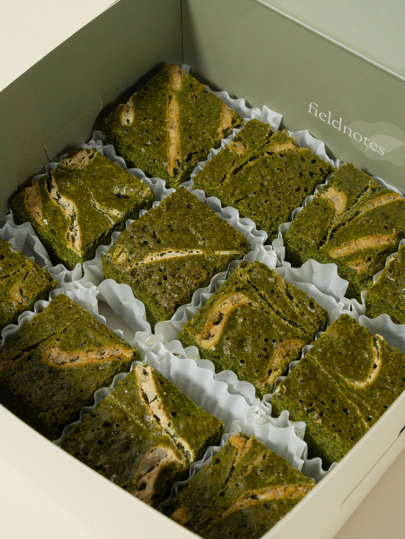 A box of 12 or 20 matcha white chocolate brownies by fieldnotes, nestled in liners in a pale green box—like elegant tarts or a birthday cake for your next afternoon tea.