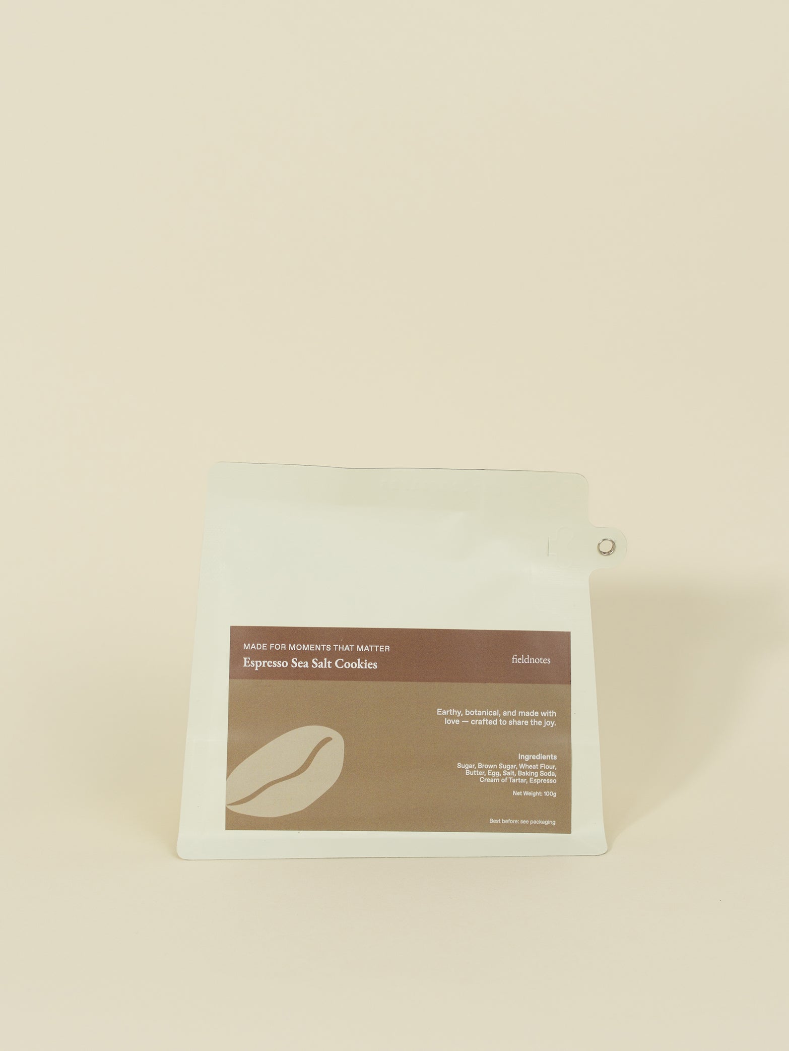 A white, resealable pouch of fieldnotes Espresso Sea Salt Cookies stands upright, its brown label resembling a customised cake or tart.