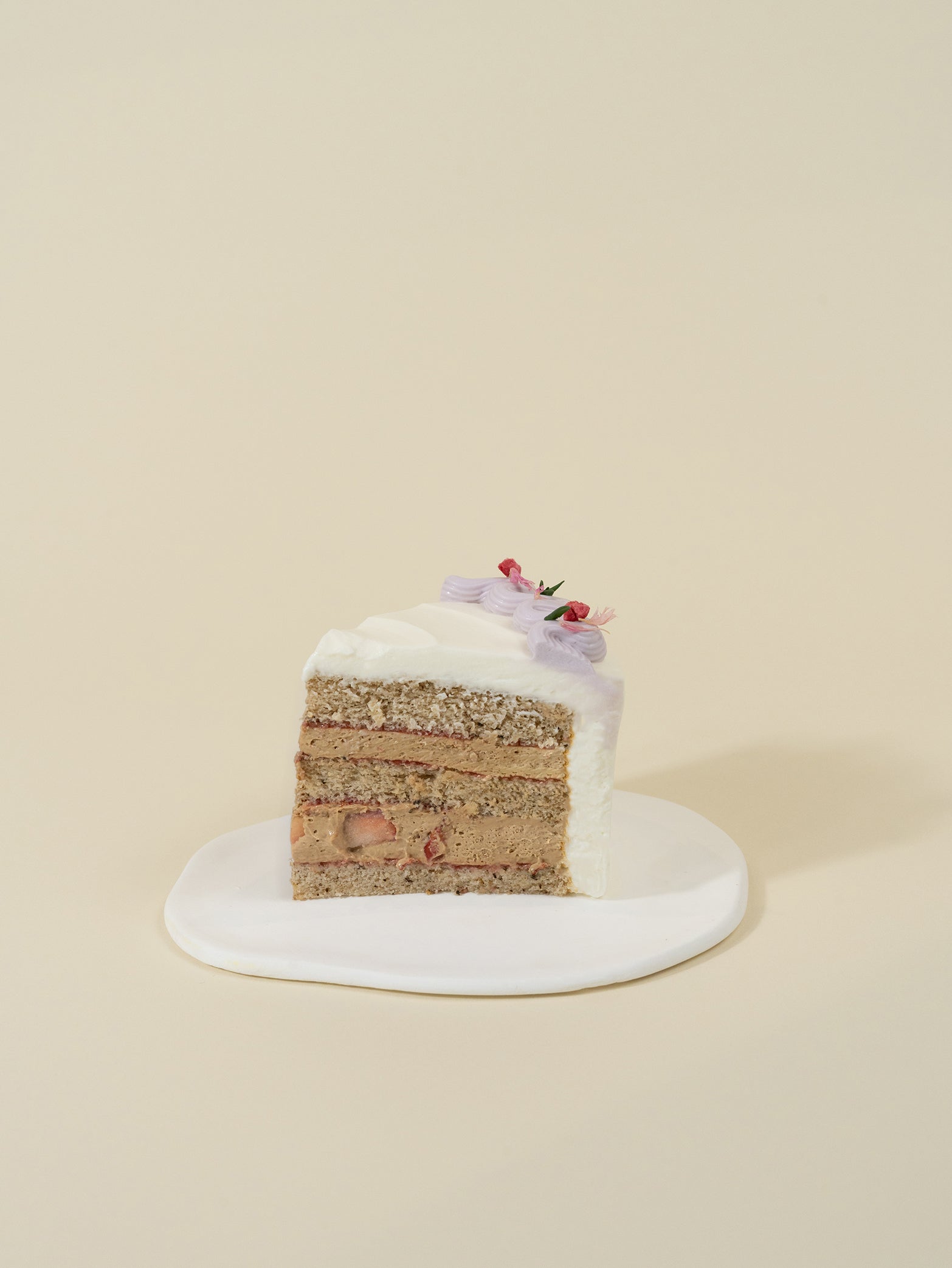 A slice of customised birthday cake—Earl Grey Wild Lavender Strawberry, with cream frosting and flowers—on a white plate, beige background.
