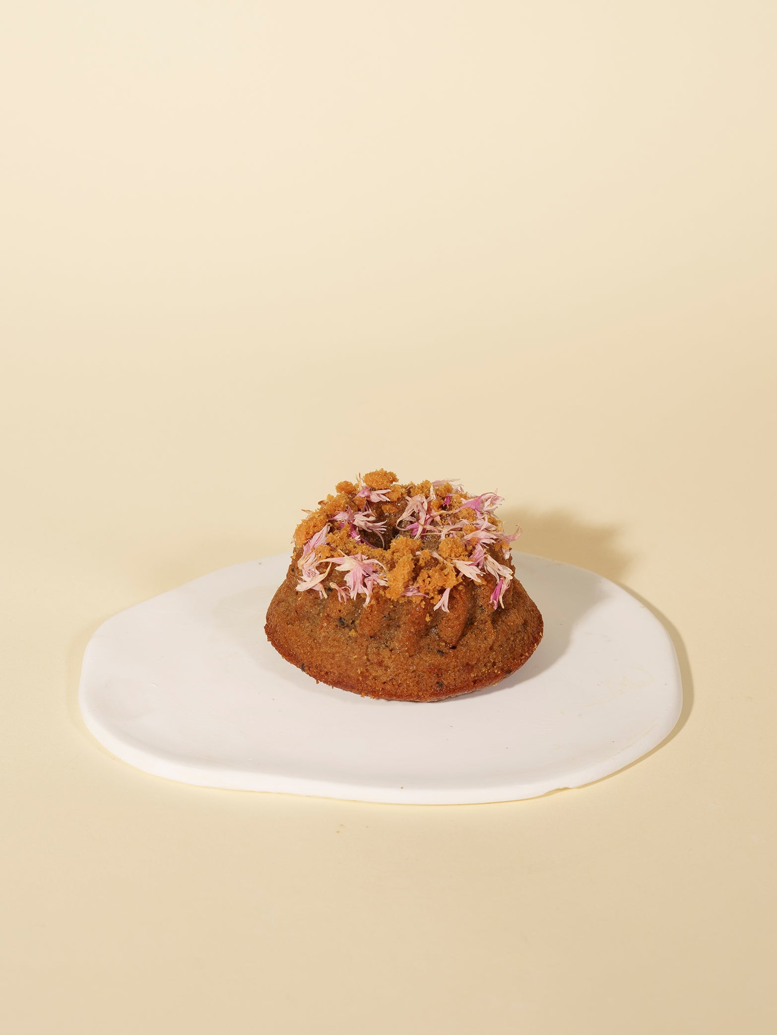 The Earl Grey Apple Tea Cake (Box of 4) by fieldnotes, like charming mini birthday cakes or tarts, topped with edible flowers on a white plate.