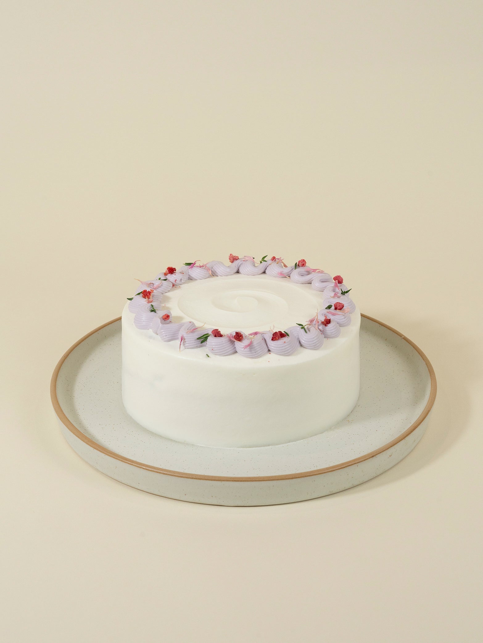 The customised Earl Grey Wild Lavender Strawberry birthday cake by fieldnotes has a round white base, light purple frosting, and strawberry toppers on a white plate with tan rim against a beige background.