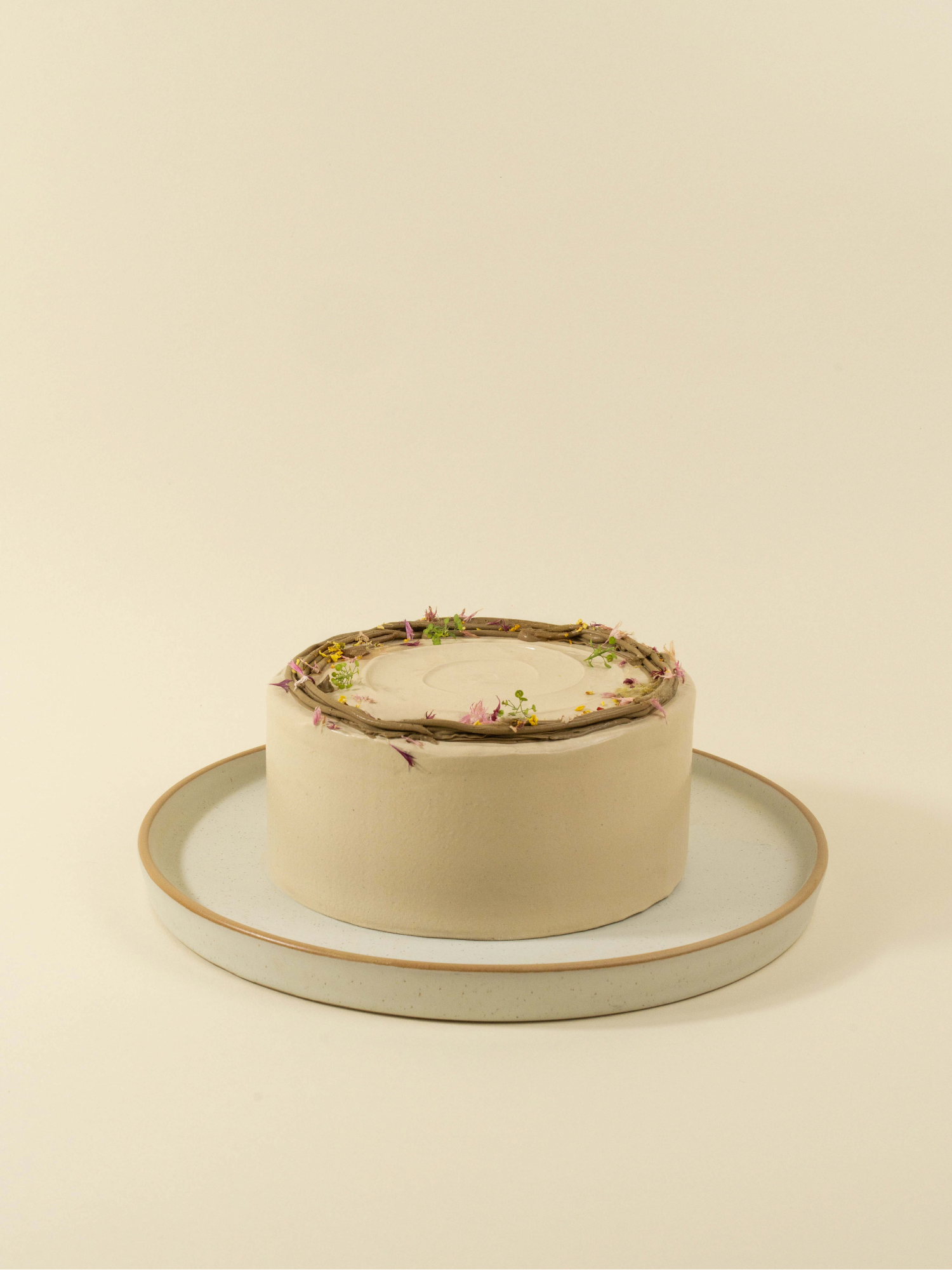 The fieldnotes Oolong Lychee birthday cake features a round, light-hued tart design with smooth frosting and floral decorations on a white plate.