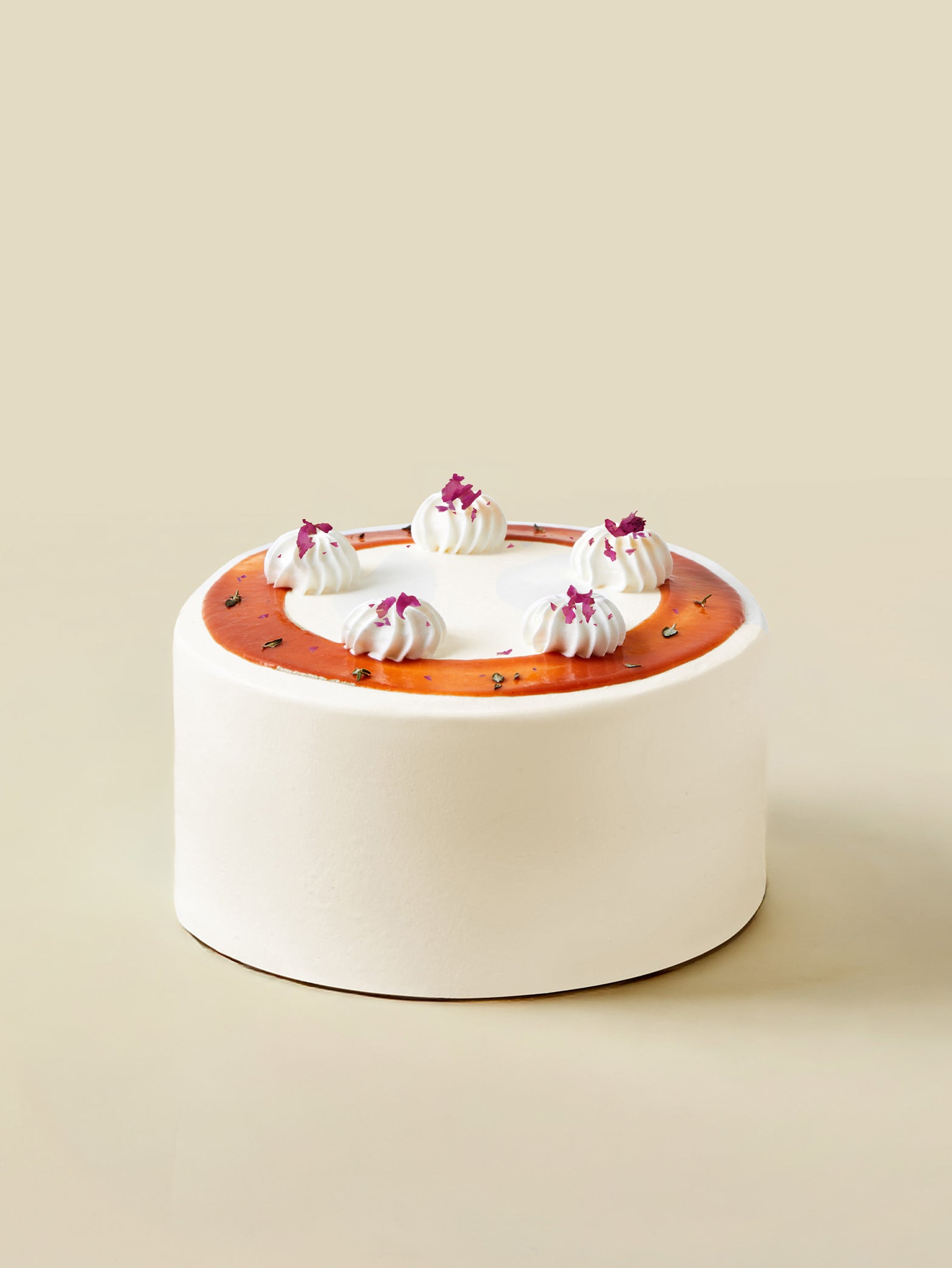 The Guava Lychee birthday cake by fieldnotes is a round, white frosted tart with caramel glaze, cream dollops, and purple petals.