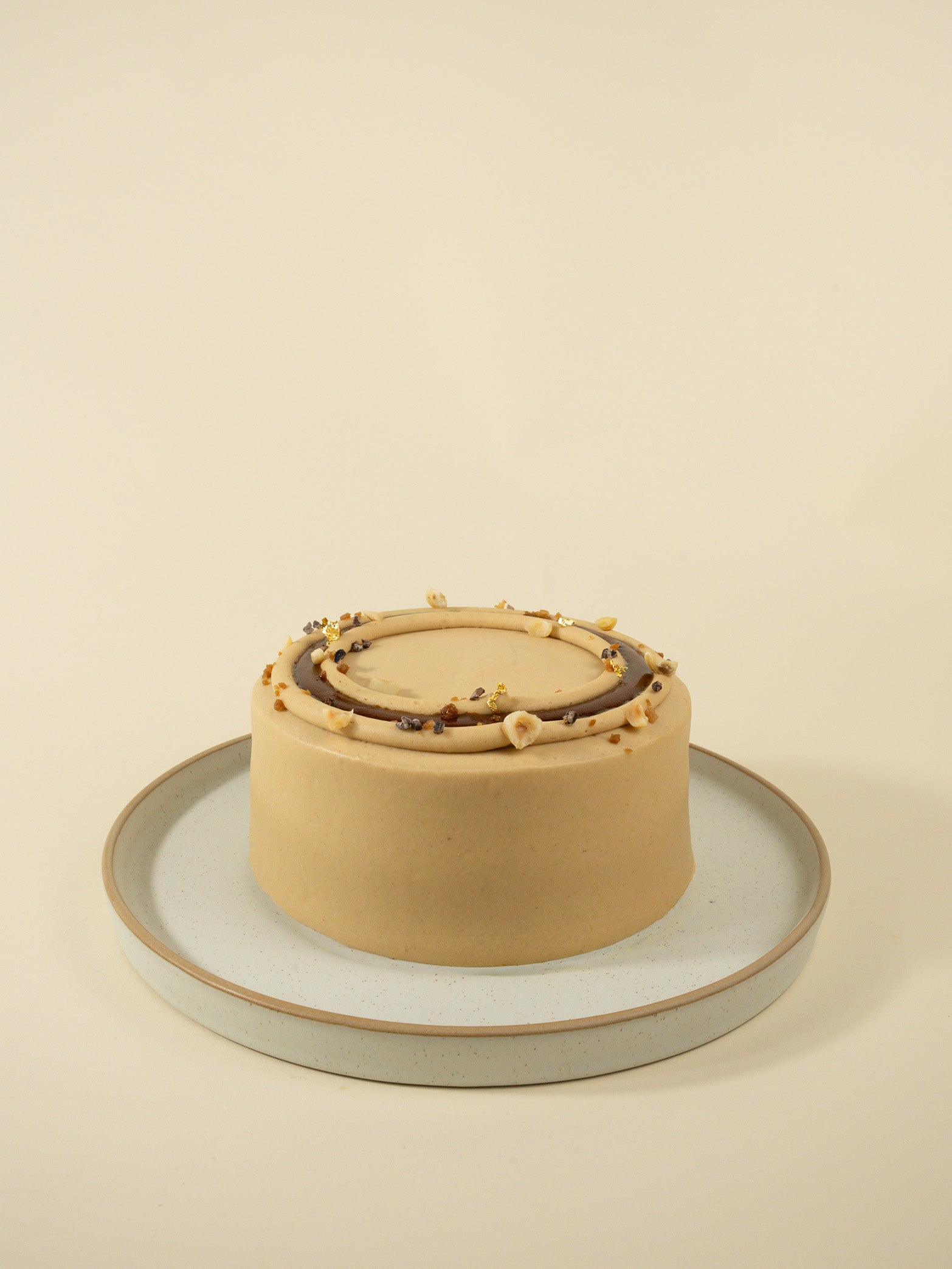 The fieldnotes Hazelnut Praline birthday cake is a small, round tart with light brown frosting, chocolate swirl, and colorful toppings.