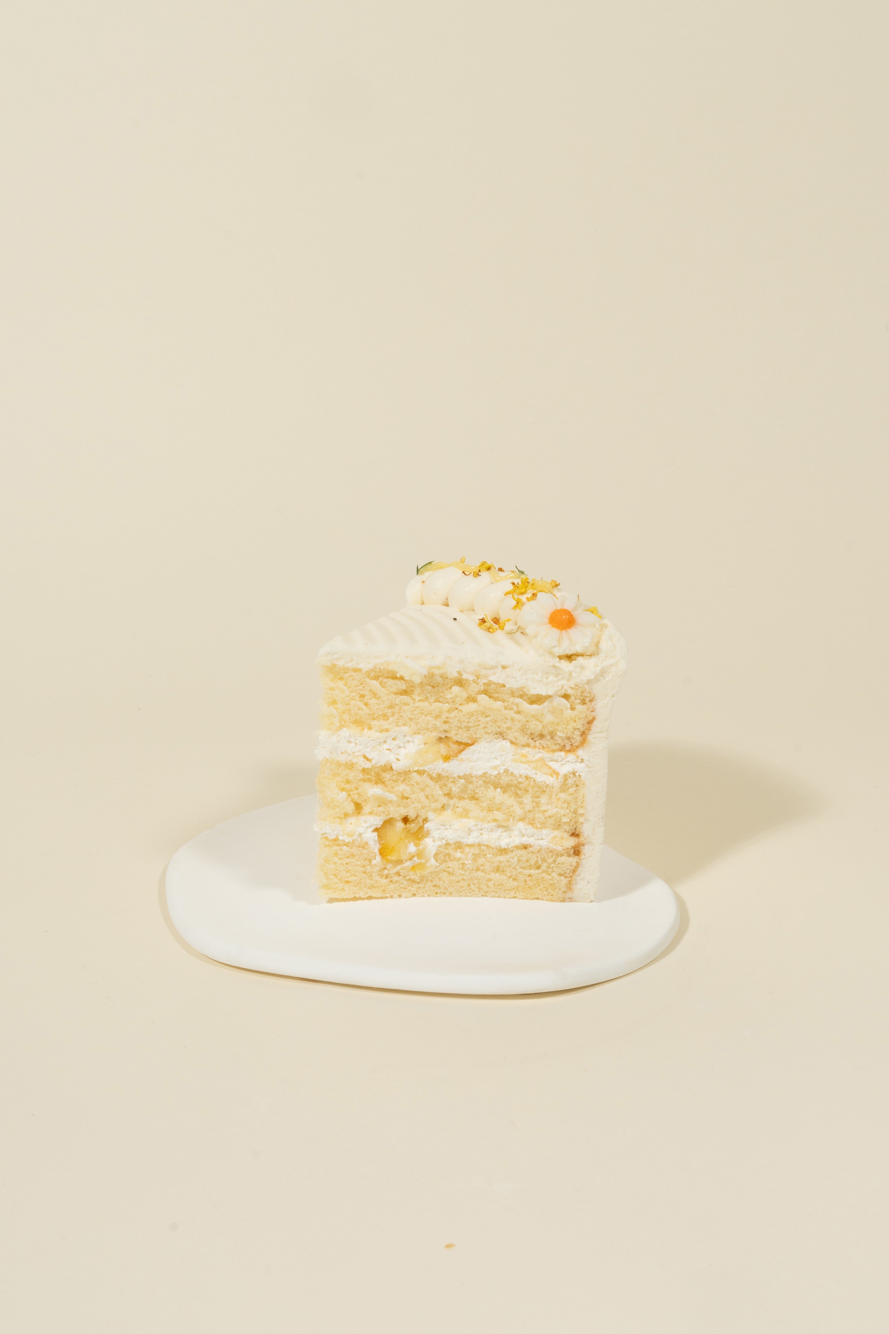 A slice of fieldnotes’ Honey Yuzu birthday cake, with vanilla sponge and Manuka Honey cream frosting, sits tart-like on a white plate.