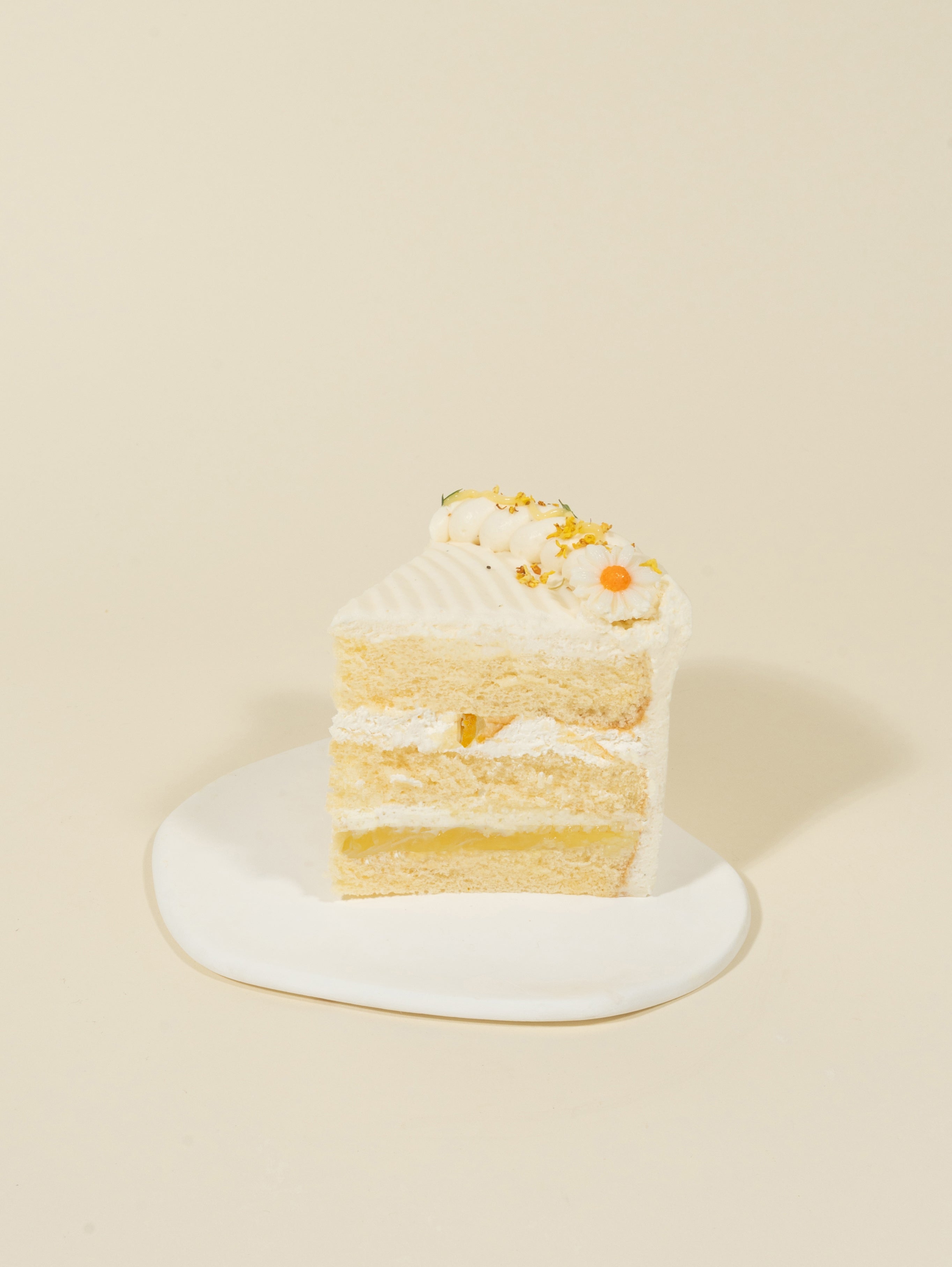 A slice of fieldnotes Honey Yuzu birthday cake with floral decorations and honey cream sits on a white plate, tart-like and elegant.