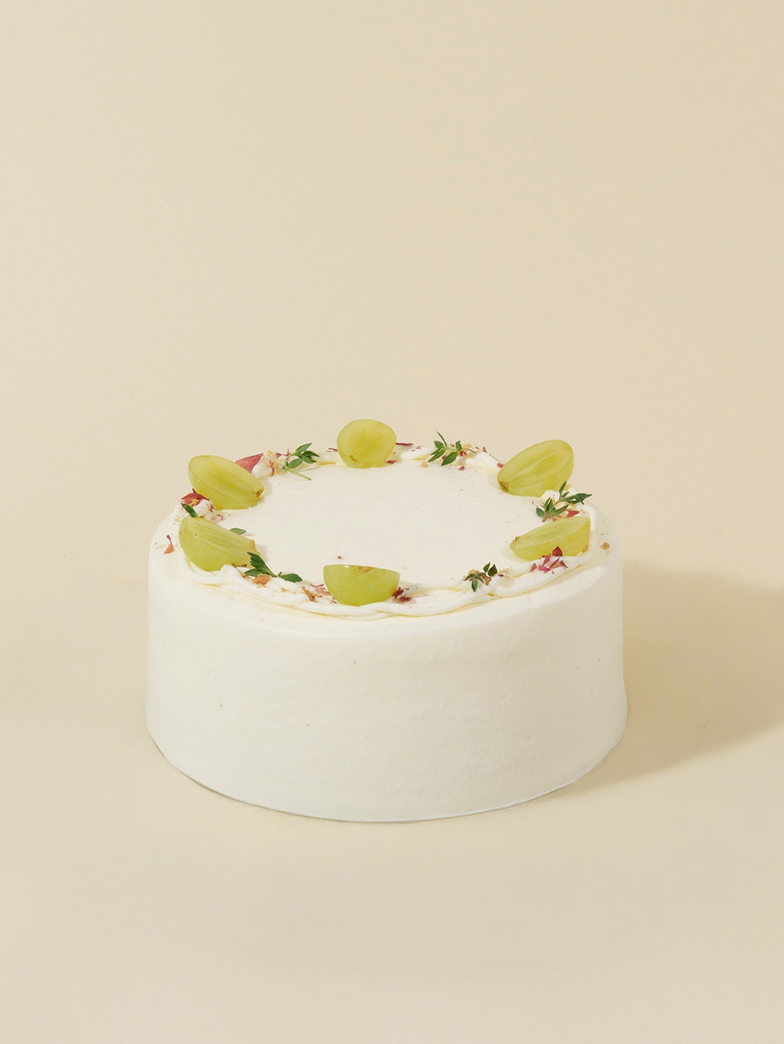 The Jasmine Grape birthday cake by fieldnotes features white frosting, halved green grapes, and herb sprigs on a plain beige background.