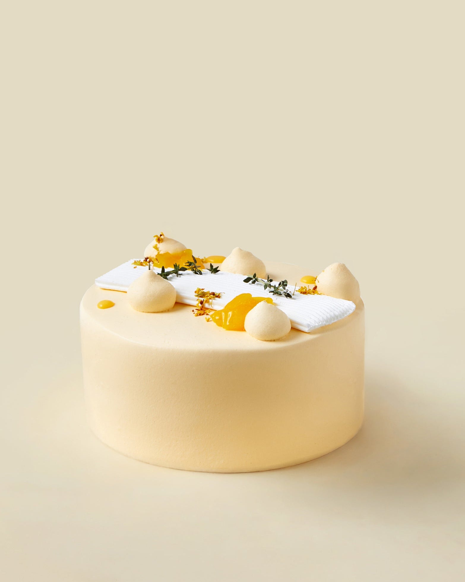 The fieldnotes Mango Yuzu | Next Day Delivery birthday cake or tart has a smooth, round, pale yellow finish with mango cream dollops, small yellow flowers, and a white garnish on a plain beige background.