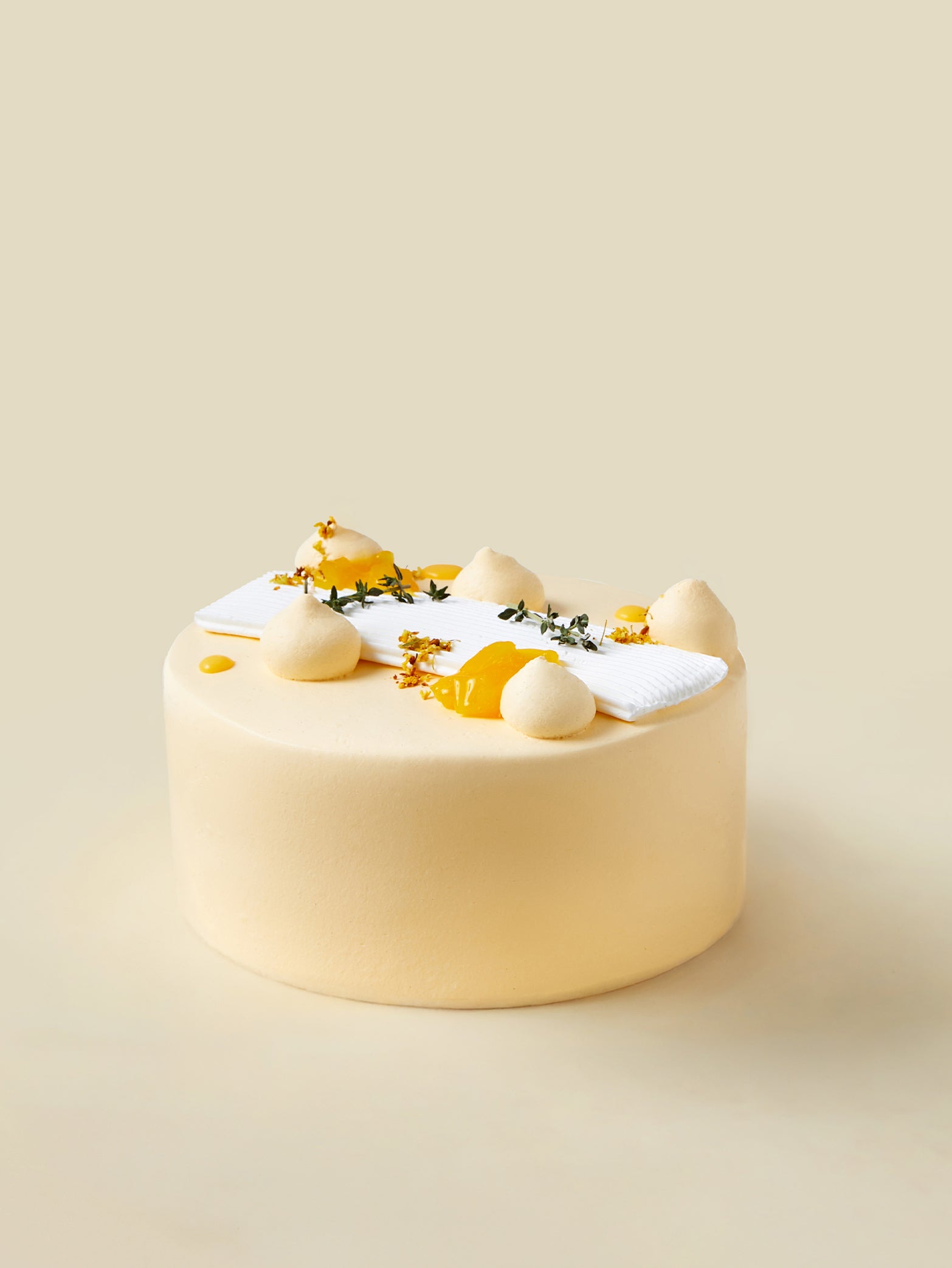 The fieldnotes Mango Yuzu | Next Day Delivery birthday cake or tart has a smooth, round, pale yellow finish with mango cream dollops, small yellow flowers, and a white garnish on a plain beige background.