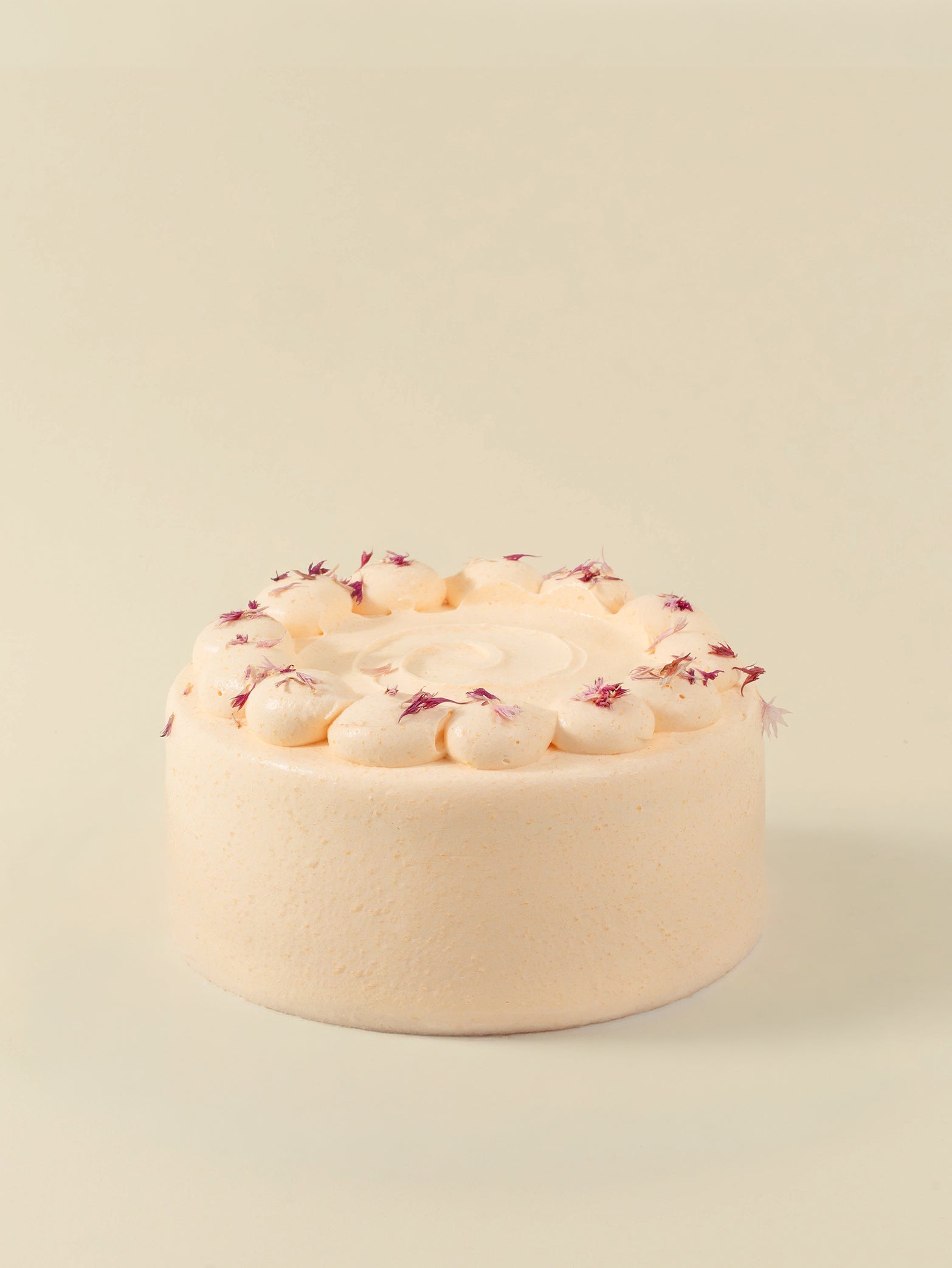 The fieldnotes Melon Lychee birthday cake boasts a round, light peach hue, tart-like smooth sides, piped swirls, and pink flowers.