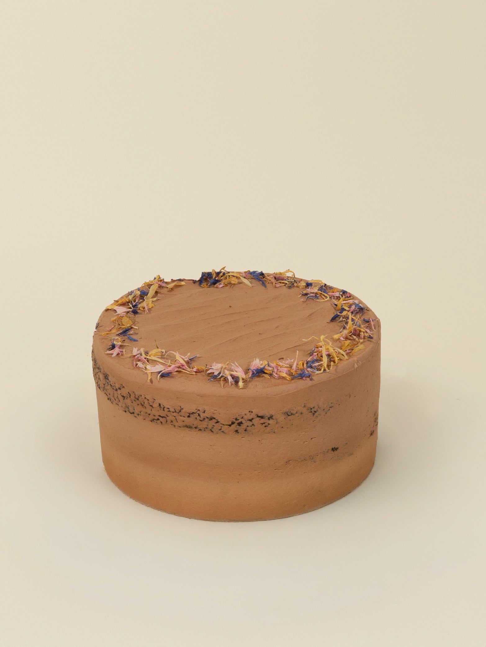 The fieldnotes Vegan Double Chocolate Cake | VEGAN is a birthday cake with smooth frosting, topped like a tart with colorful dried flowers. It sits on a plain light surface against a beige background.