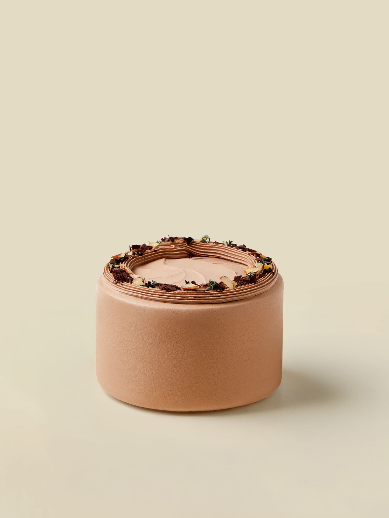 The fieldnotes All Chocolate birthday cake is round, smooth with textured sides, ganache topping, flowers and leaves decor, on beige.