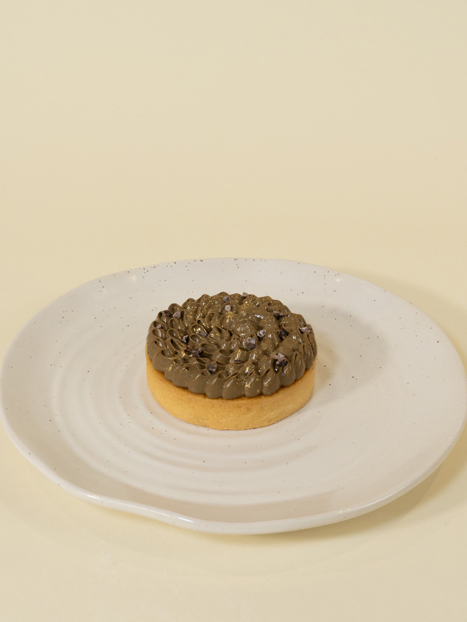 The Kyoto Hōjicha Tart (8CM box of 3) features a round tart with swirled chocolate cream and gold dust atop a white ceramic plate, its refined look inspired by the subtle elegance of Kyoto Hōjicha.