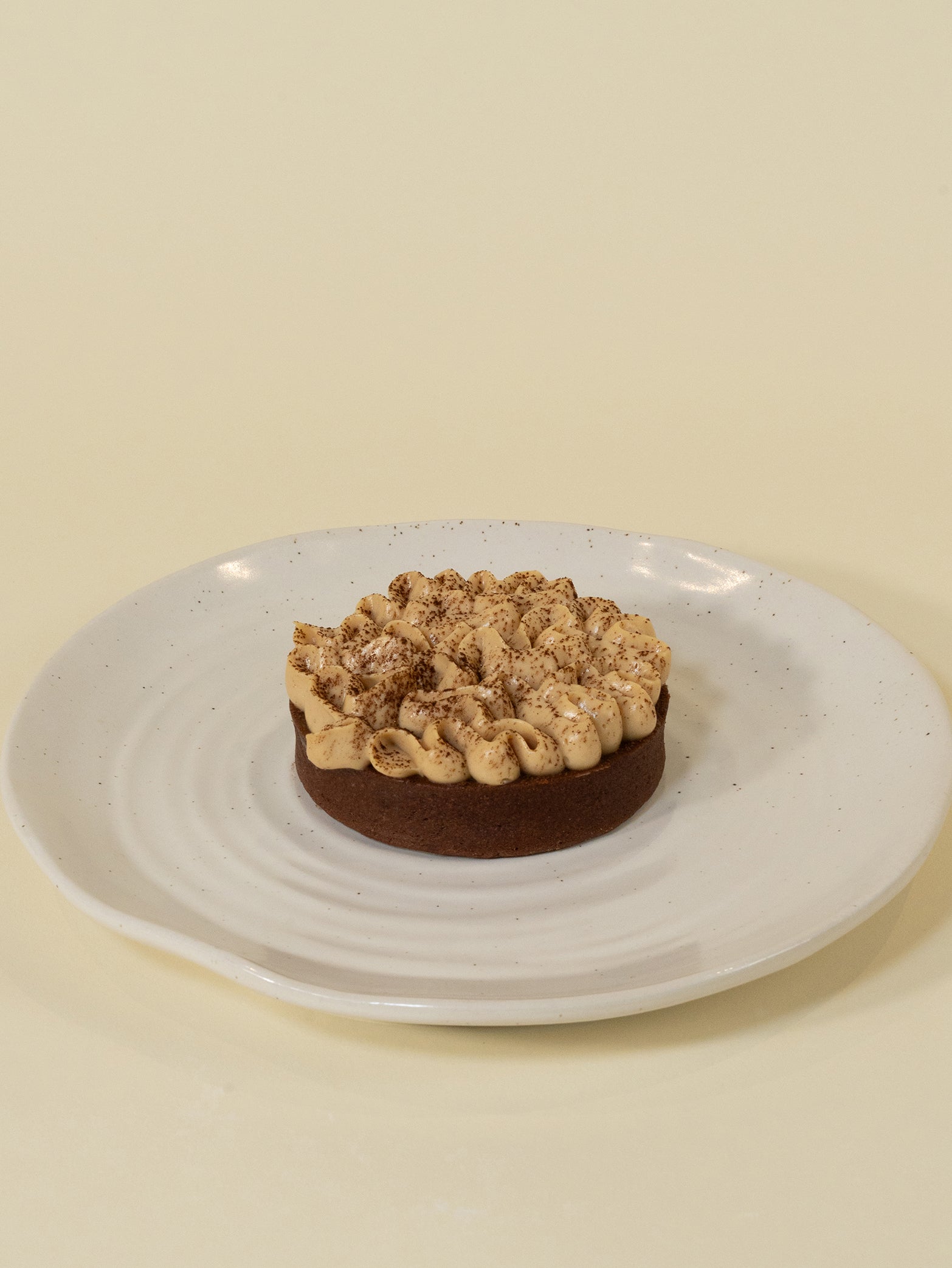 The birthday tart features layers of chocolate ganache and hazelnut praline crunch, topped with cream and cocoa, on a white plate.