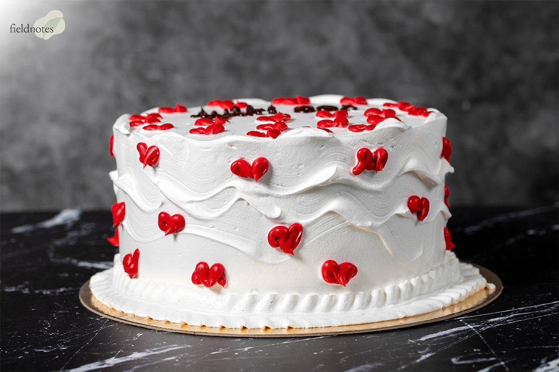 White frosted cake decorated with red cream hearts.