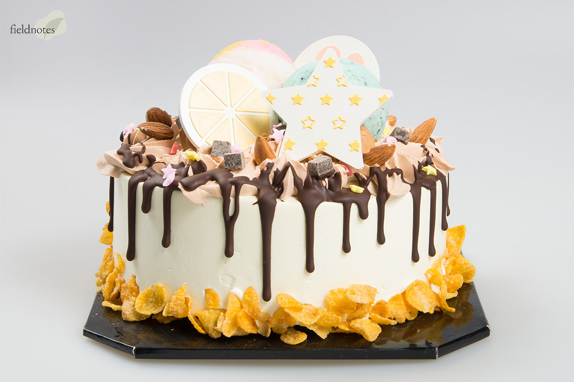 Decorated white cake with chocolate drips, macarons, almonds, candy, and a star cookie on top