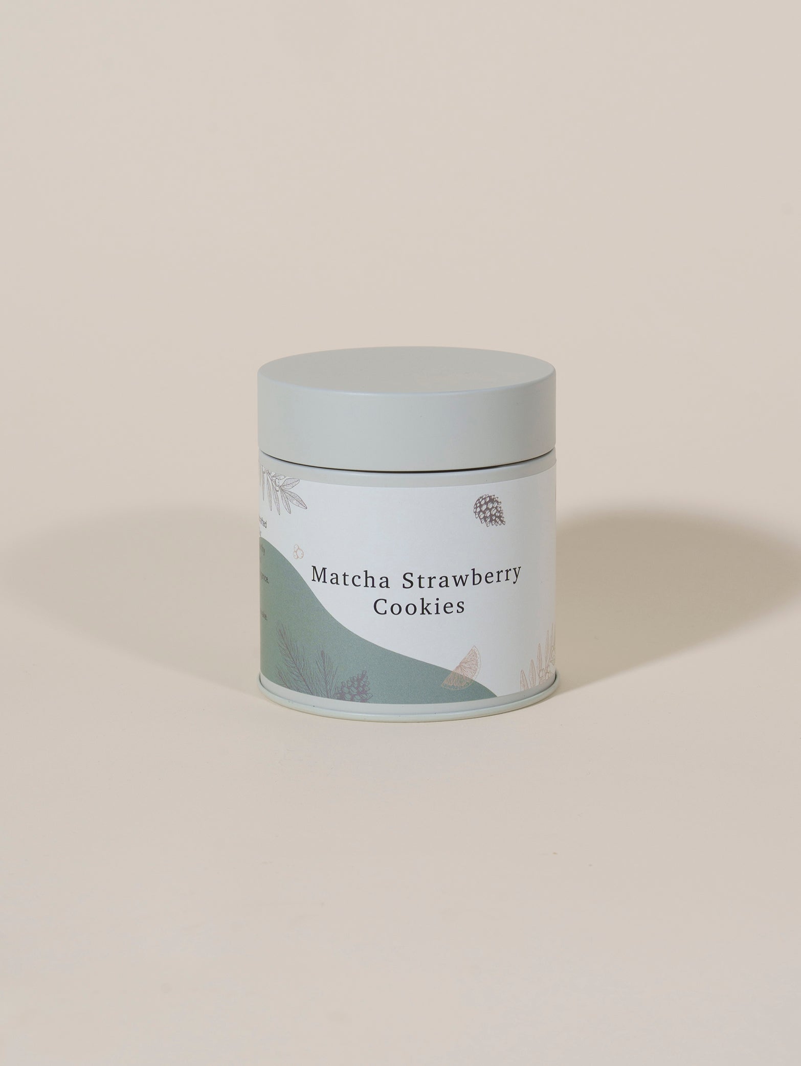 A light green cylindrical tin from fieldnotes, labeled “Matcha Strawberry Cookies,” stands on a plain background, its subtle botanical label hinting at handcrafted treats reminiscent of birthday cake or strawberry tart.