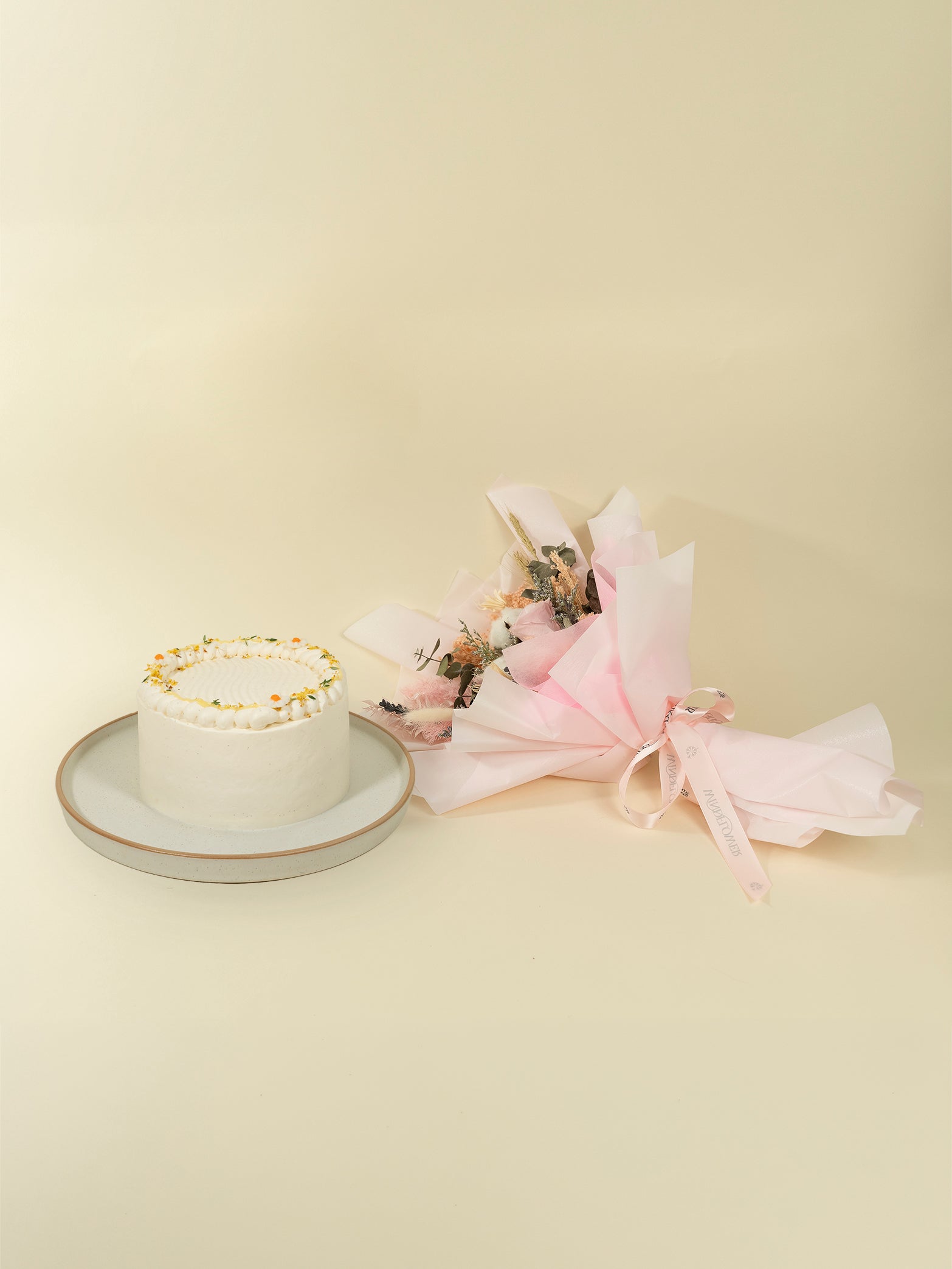 The Fieldnotes x Windflower Florist Bundle includes a 15CM birthday cake with white frosting beside a tart-pink wrapped bouquet on a plate.