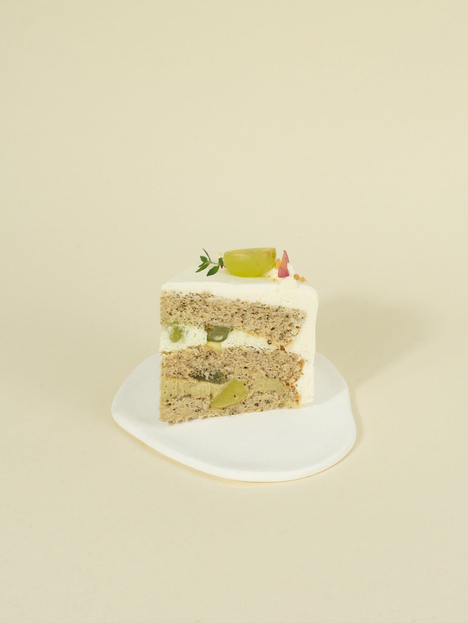 A slice of Jasmine Grape birthday cake by fieldnotes features white frosting and grape pieces, like a tart, on a white plate.