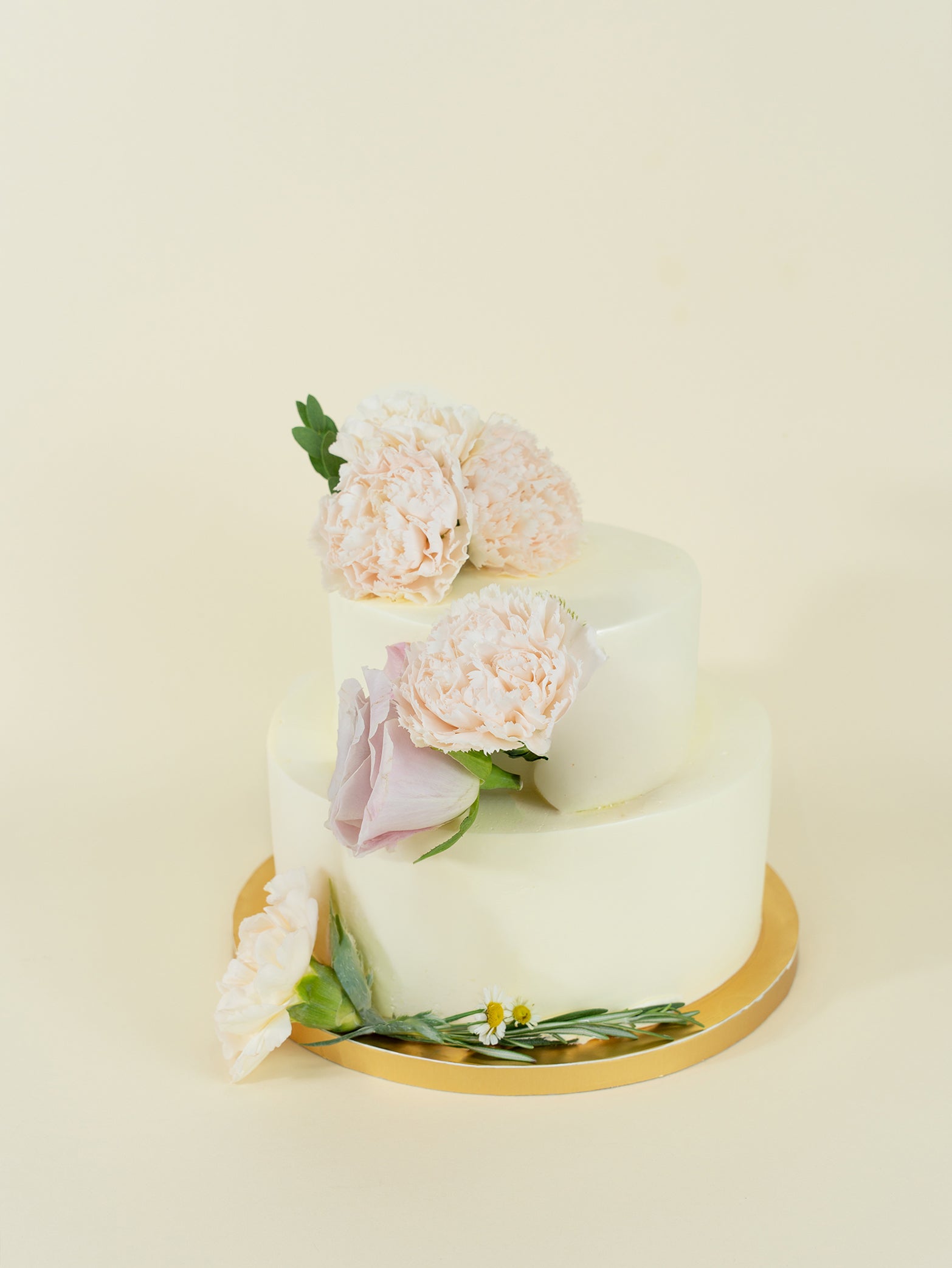 The fieldnotes [5 days in advance] Minimalist Sunburst birthday cake is a two-tiered buttercream tart with pale pink and purple flowers, on a gold board against a light cream backdrop.