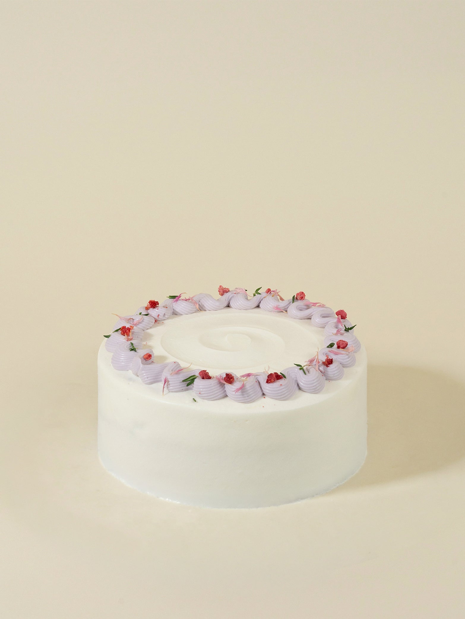 The Fieldnotes birthday cake is round, white frosted, with light purple borders and red flowers, shown on a light beige surface.