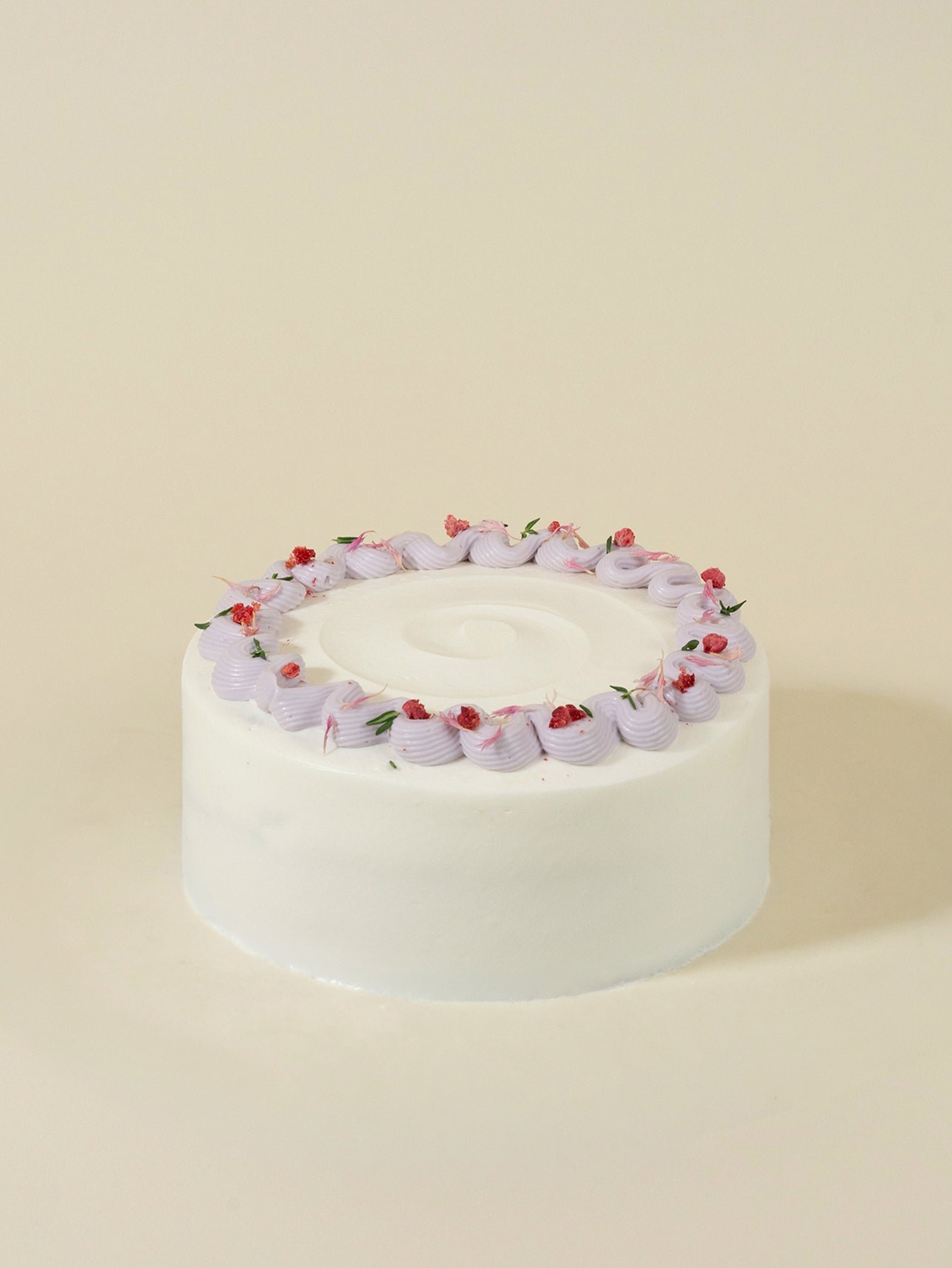 The birthday cake features a round white frosted finish, topped with light purple swirls and pink petals like a delicate tart.
