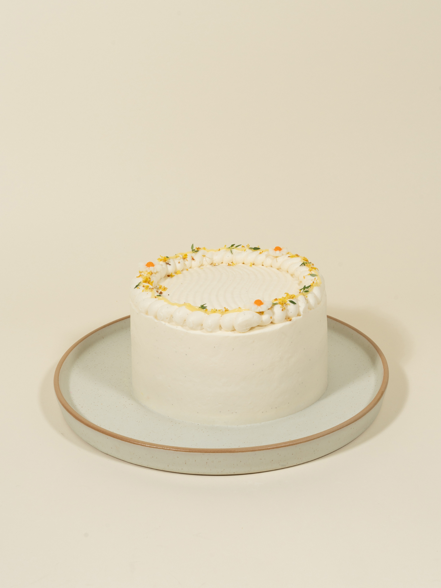 The Honey Yuzu birthday cake by fieldnotes is frosted white, topped with yellow and white flowers, served on a gray plate.