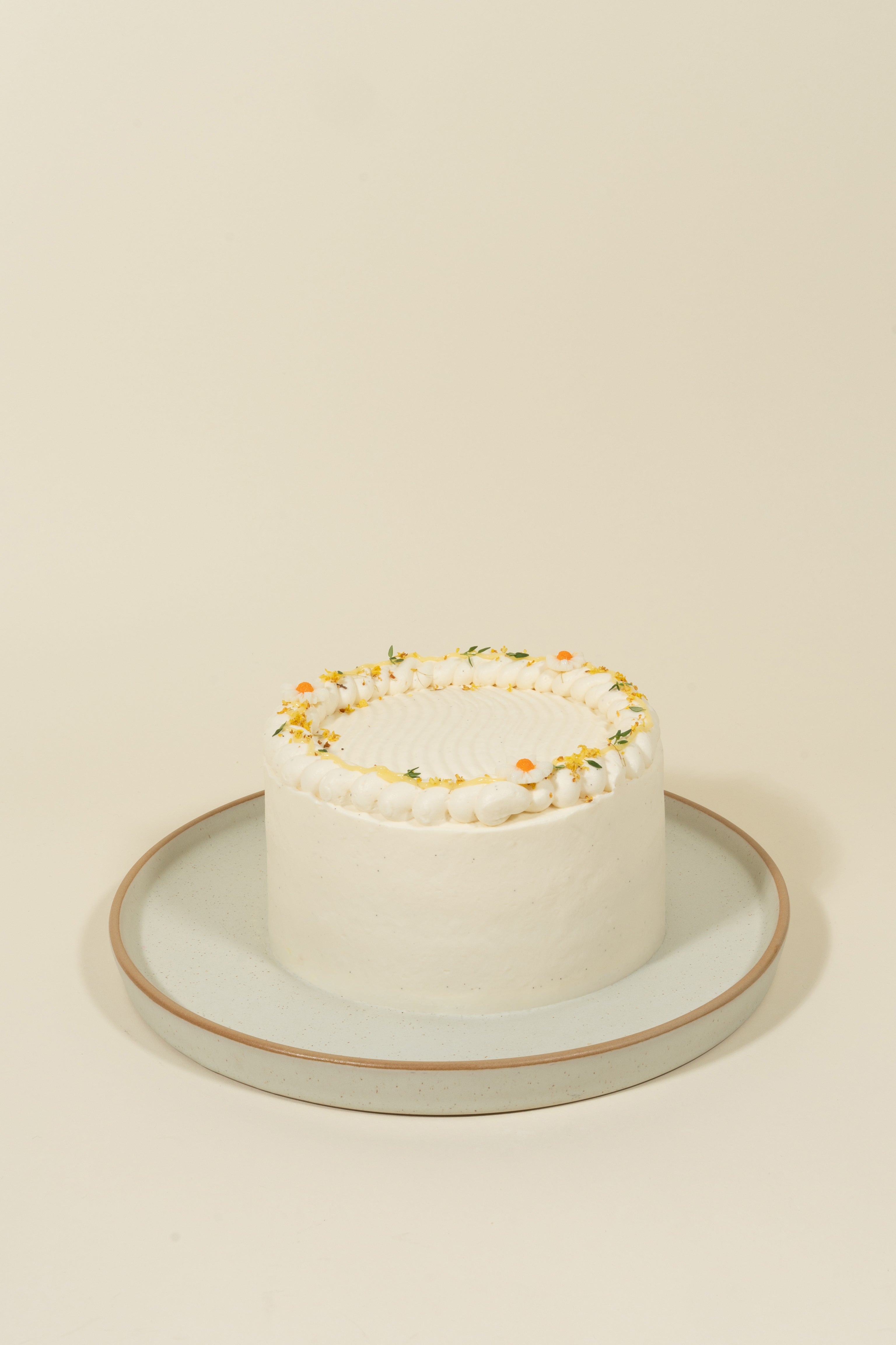 The Classic Cakes (Party Size) by fieldnotes is a small, round white birthday cake or tart with simple frosting and yellow-white flower accents on a light gray plate—perfect for pairing with fine teas.