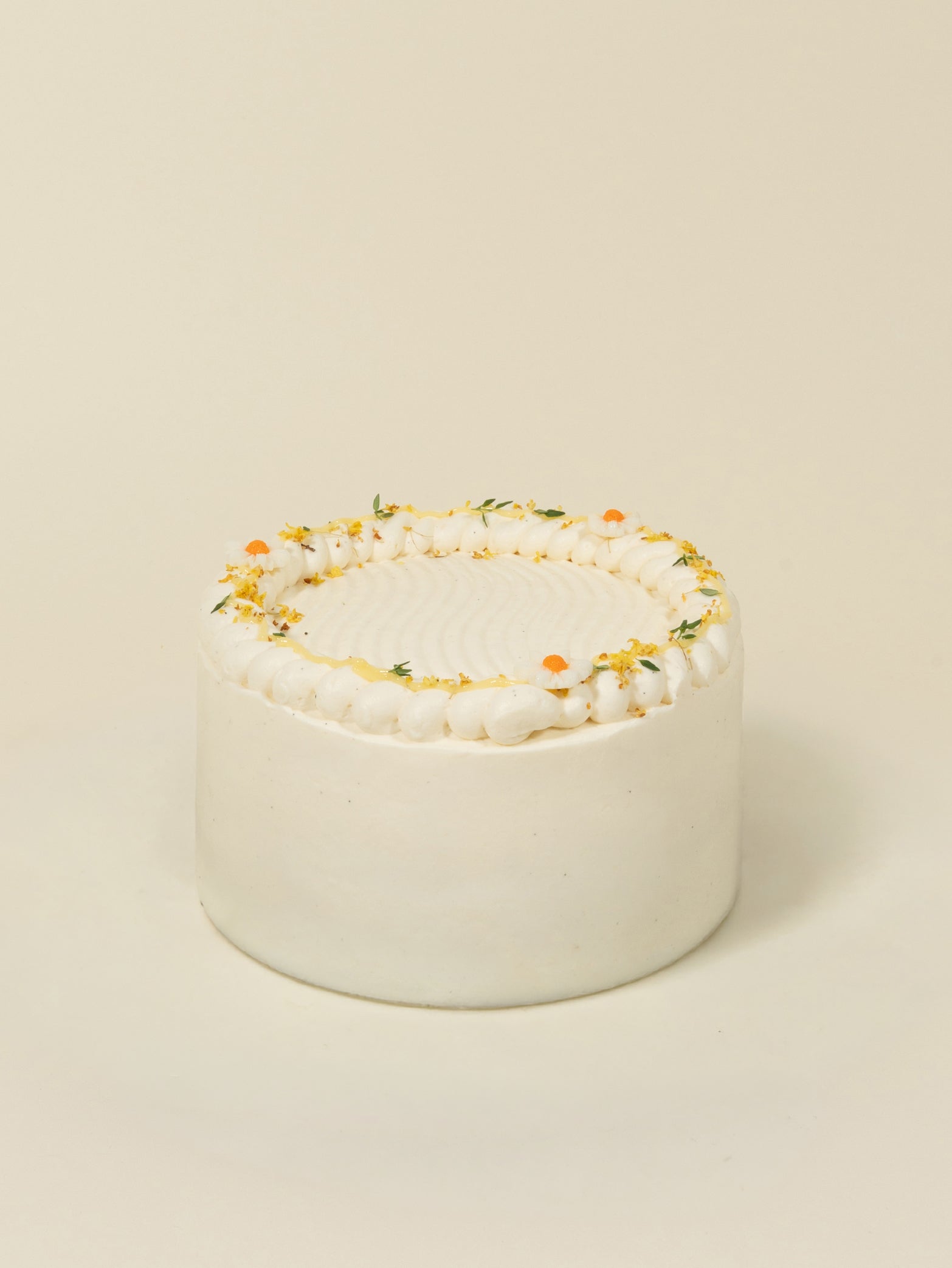The fieldnotes Honey Yuzu | Next Day Delivery is a small, round white cream birthday cake or tart with smooth frosting, piped cream, and orange and yellow floral accents on a plain beige background.