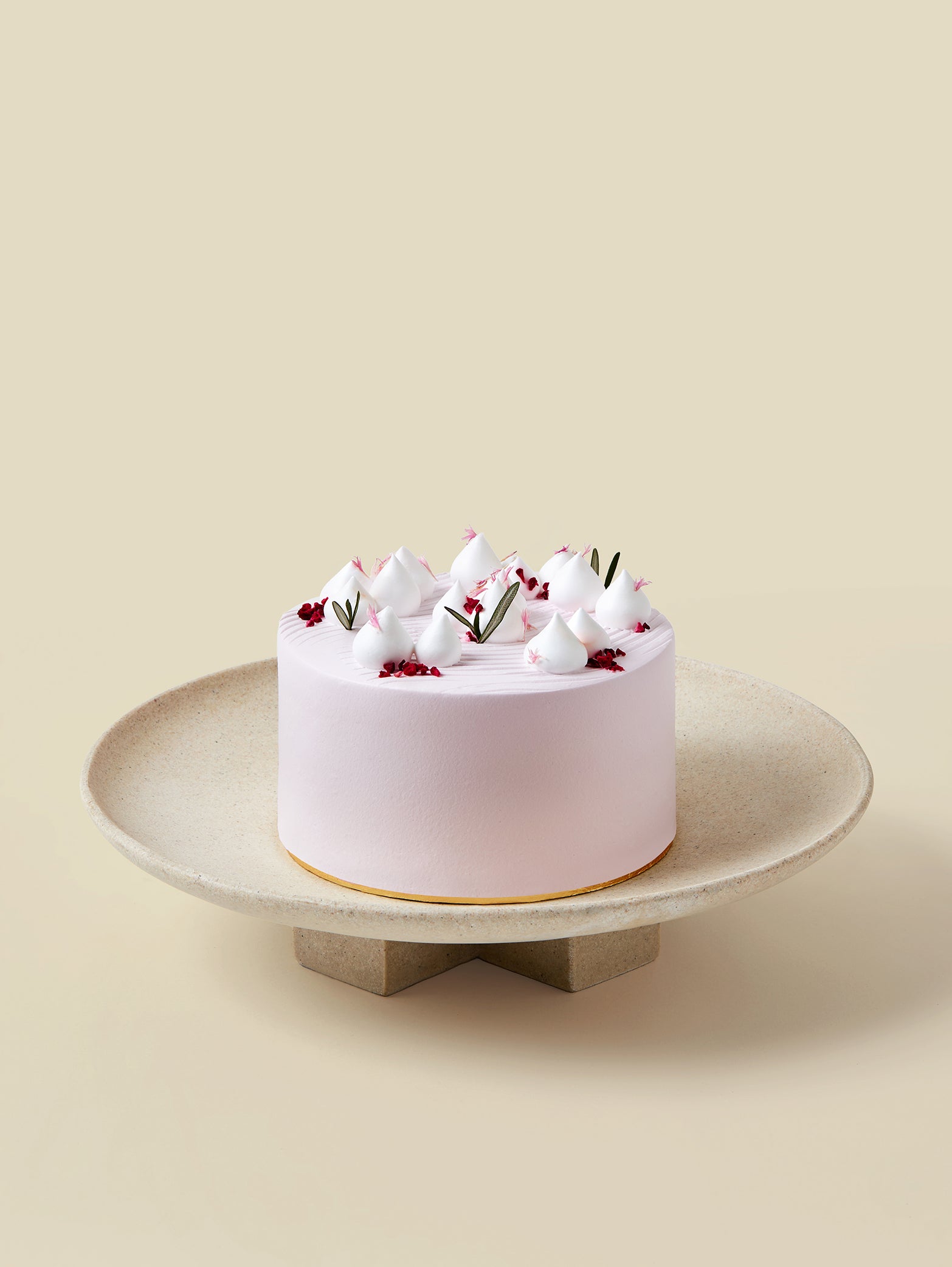 The fieldnotes Classic birthday cake (Party Size) features light pink frosting on a beige stand, with meringue peaks and floral tart decor.