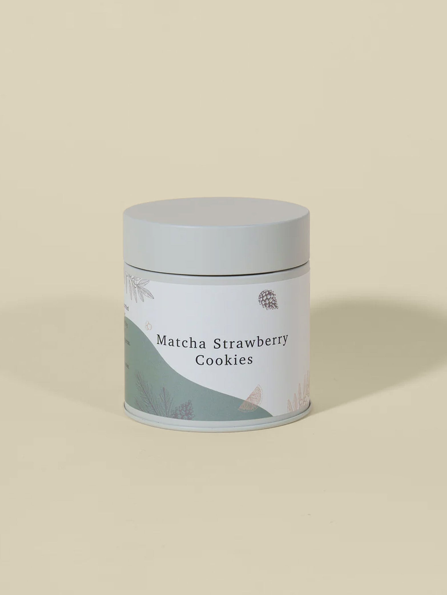A cylindrical tin from fieldnotes with a gray lid and pastel label reading Matcha Strawberry Cookies or Birthday Cake Tart, on beige.