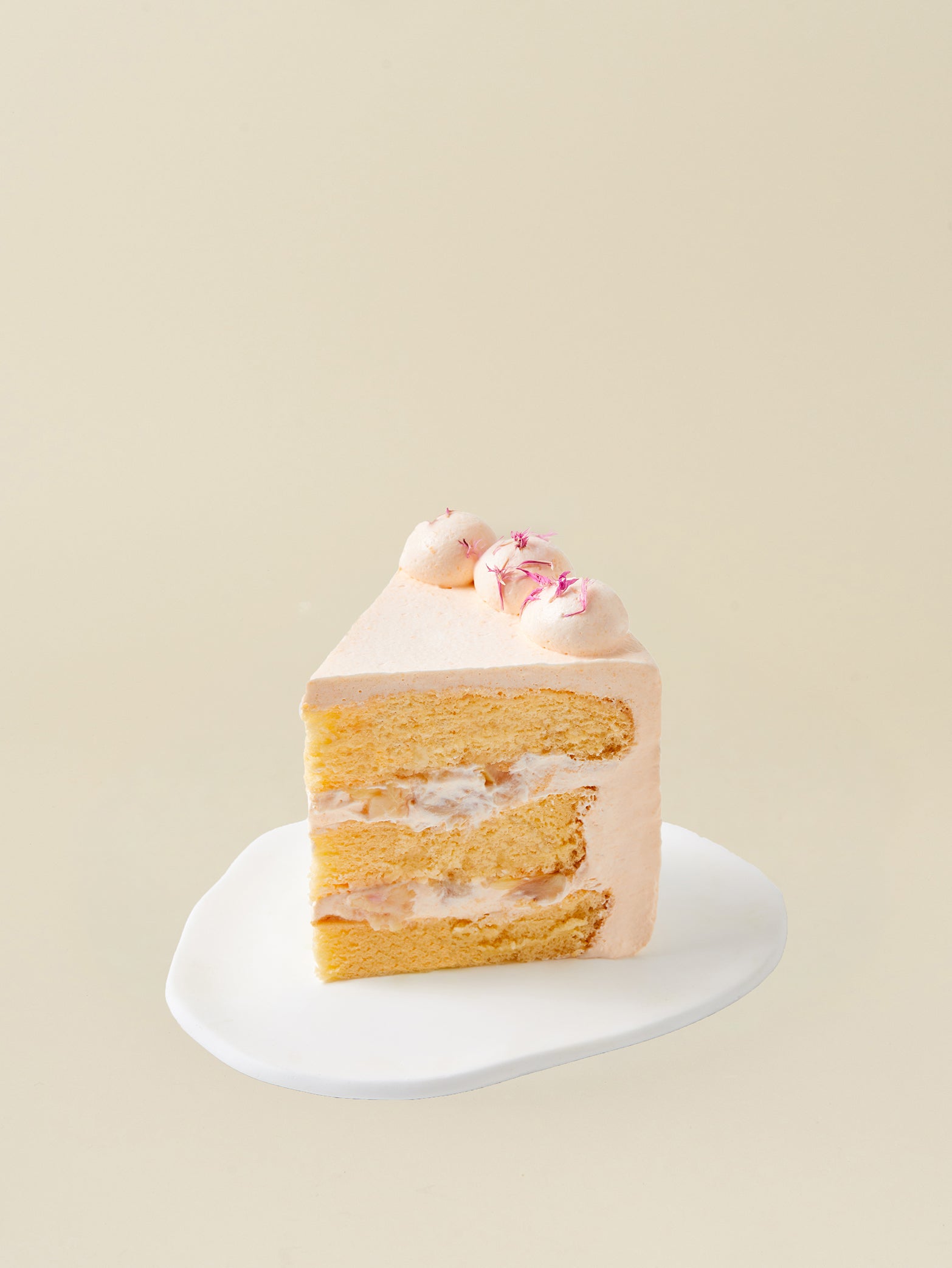 A slice of fieldnotes Melon Lychee birthday cake, with light pink frosting and tart lychee layers, sits on a white plate.