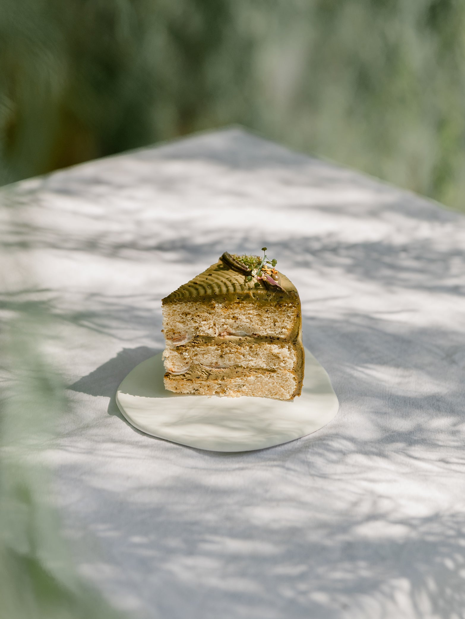 A slice of birthday cake-inspired fieldnotes Oolong Lychee tart with green frosting rests on a white plate, bathed in gentle natural light.