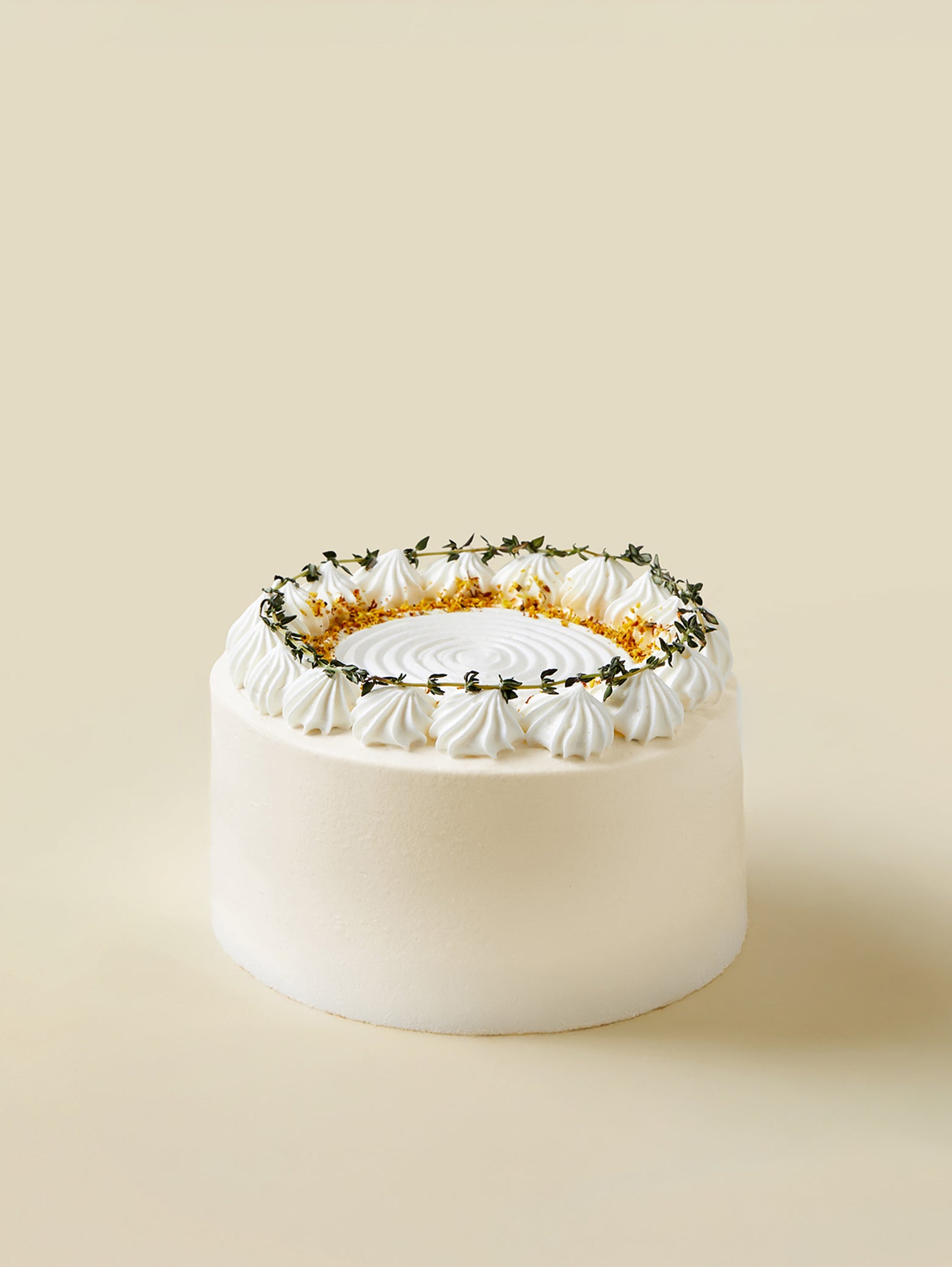 The fieldnotes Passionfruit Jasmine birthday cake is a round tart with white frosting, piped swirls, green sprigs, and gold flakes.