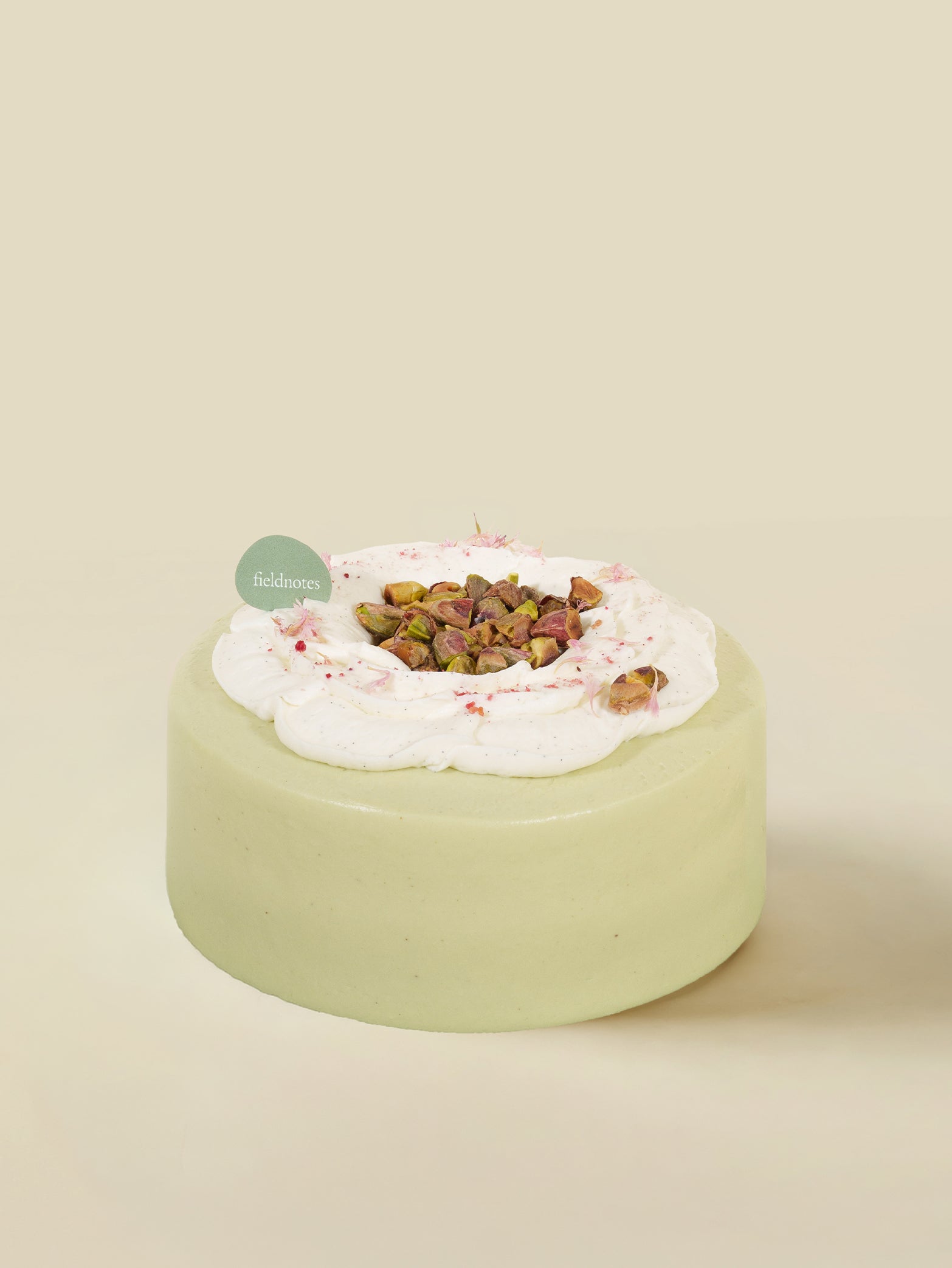 The Pistachio Praline birthday cake by fieldnotes is a smooth, round tart topped with white cream, pistachios, and a green label.