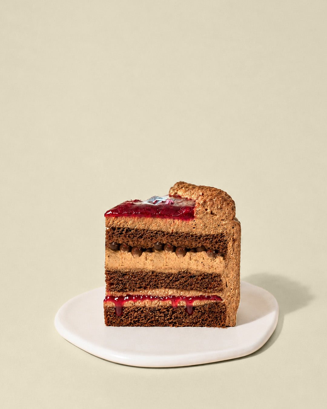 A slice of Berryglass birthday tart, layered with chocolate cream and red fruit jam, sits on a white plate against a beige background.