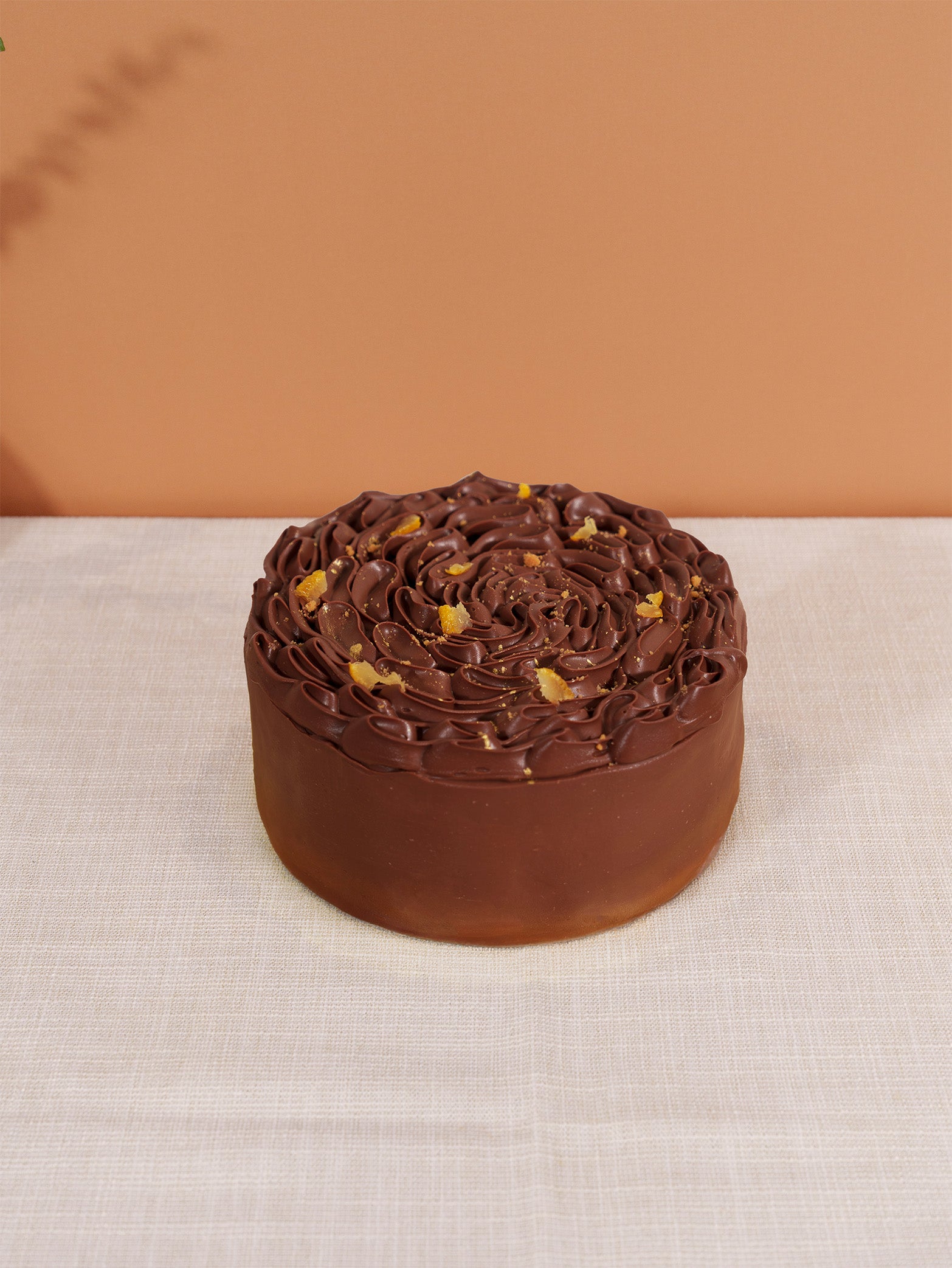 A round birthday cake made with fieldnotes Yuzu Caraïbe 66% chocolate, swirled frosting, orange garnish, on a white tablecloth.
